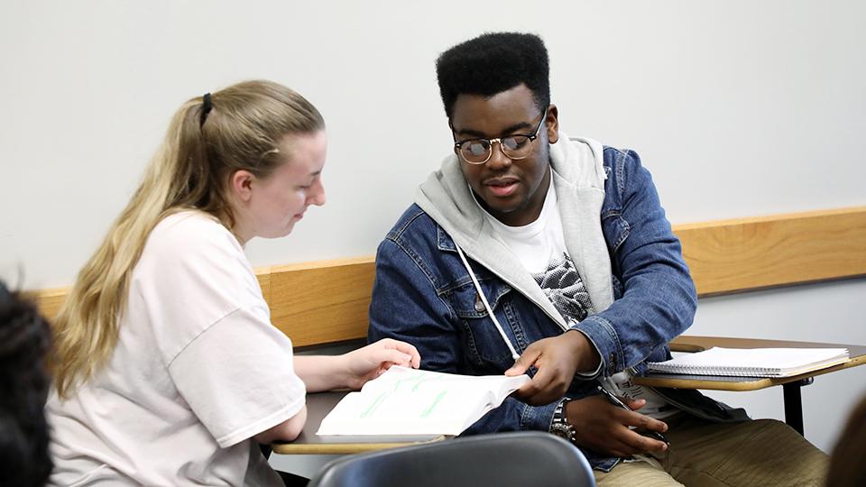 A student hands a paper to another student.